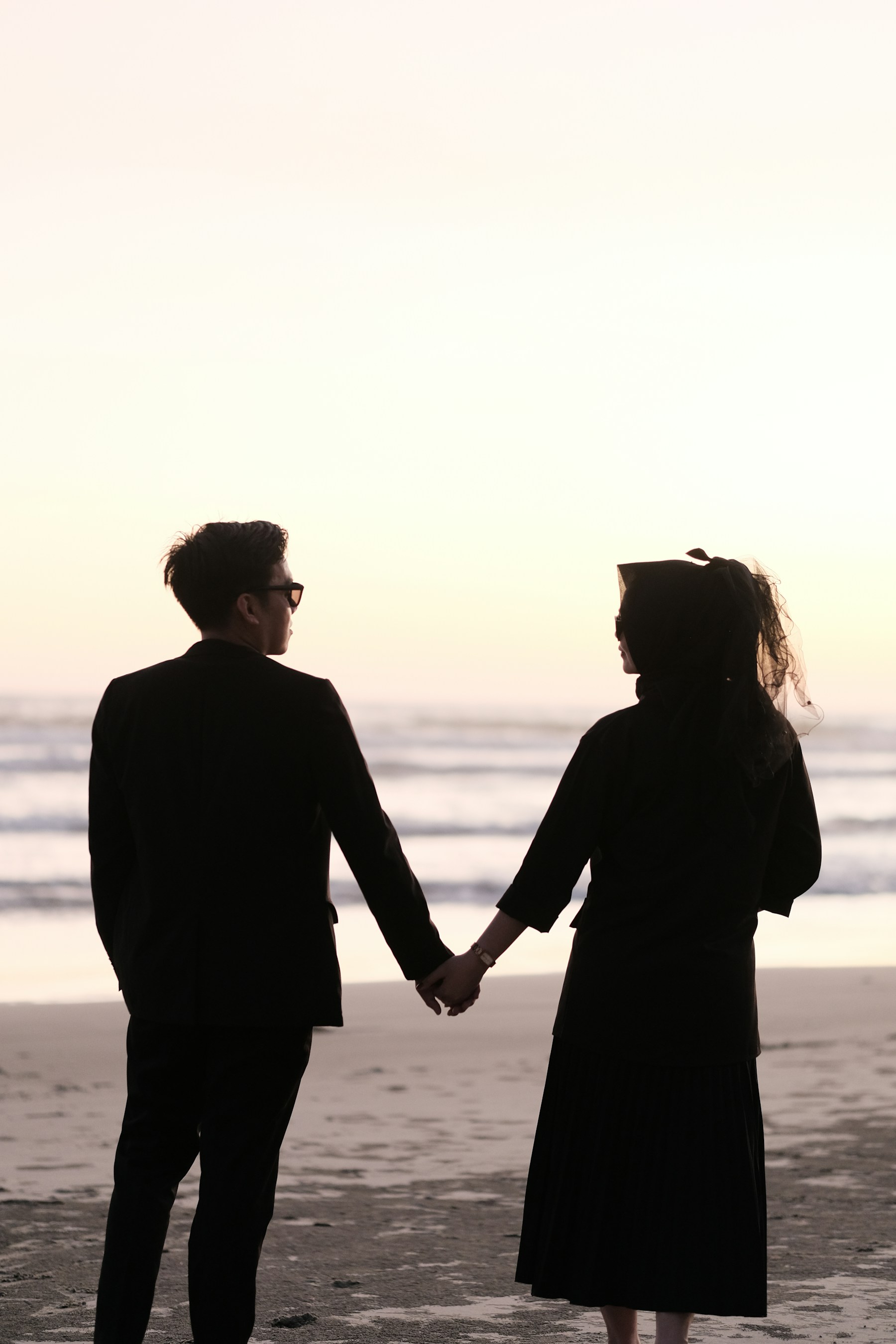 Casal de mãos dadas contemplando o pôr do sol na praia