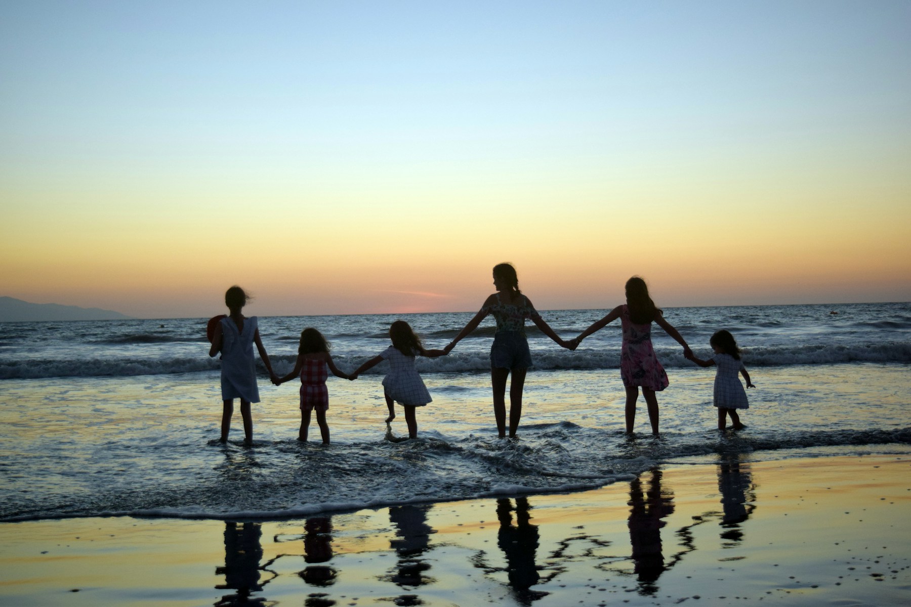 Família de mãos dadas na praia ao pôr do sol